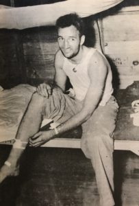 Tom Harmon sits on his bunk, tending to a minor wound